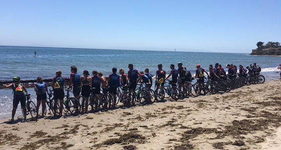 Large group of cyclists lined up on a beach with ocean in background
