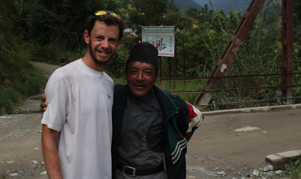 Two men smiling at camera outdoors with mountains and vegetation in background