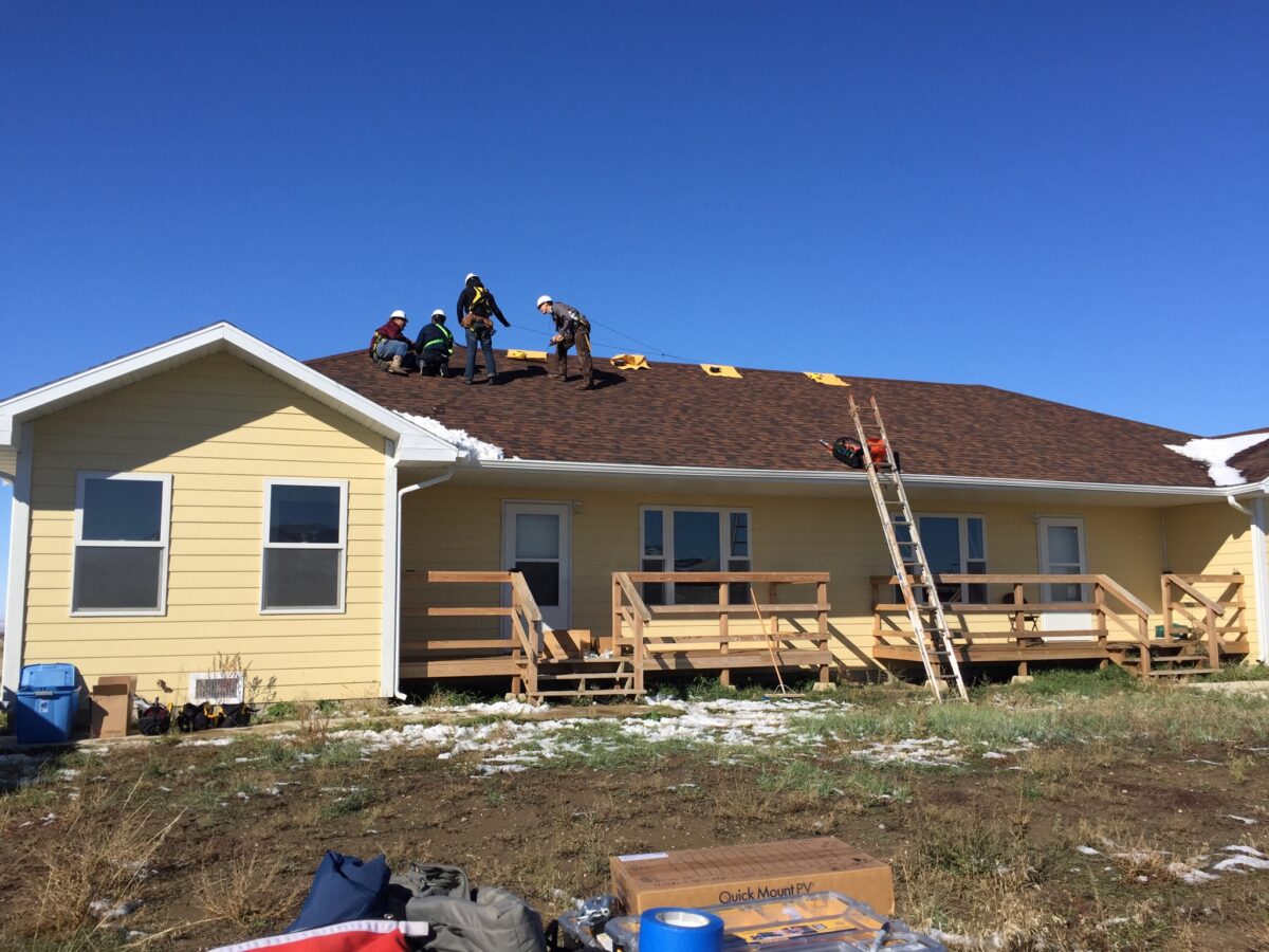 Roofing crew installing solar panels on yellow modular home in Montana under clear blue sky