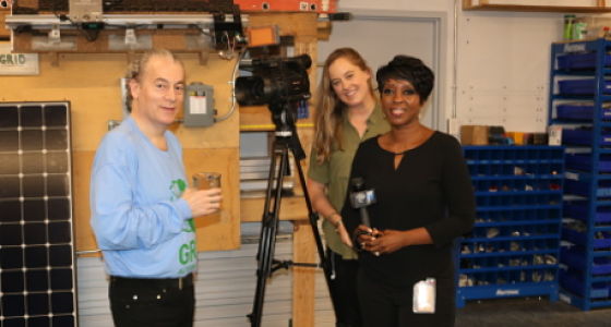 Cheryl Wills from NY1 interviews GRID Alternatives staff in workshop with solar panel and equipment visible
