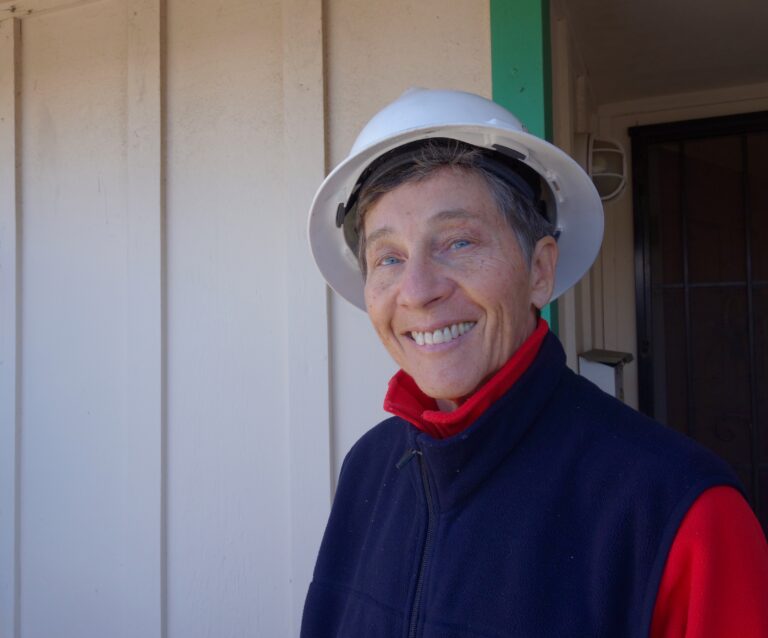 Smiling man wearing white hard hat and red-and-navy jacket standing outdoors