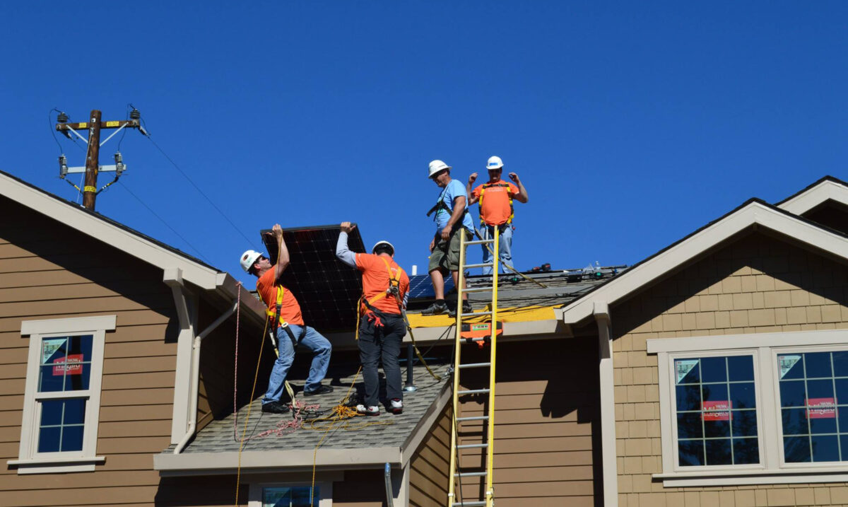 Construction workers installing solar panels on a residential roof under blue sky