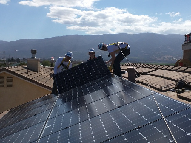 Workers install solar panels on a rooftop with mountains visible in the background