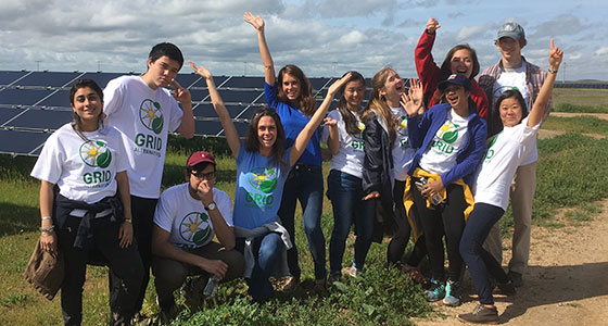 Group of smiling volunteers in GRID shirts at a solar farm site, celebrating