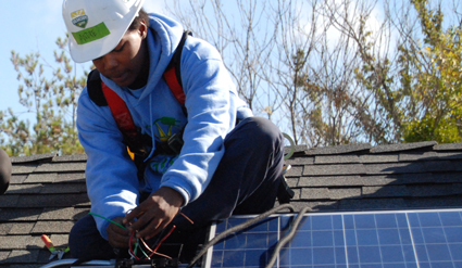 Worker in safety gear installing solar panel on residential roof