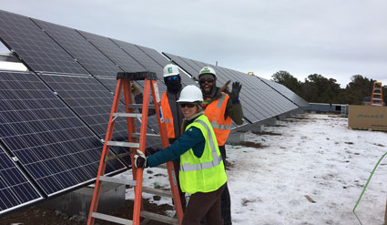 Two workers in safety gear installing solar panels on a snowy rooftop
