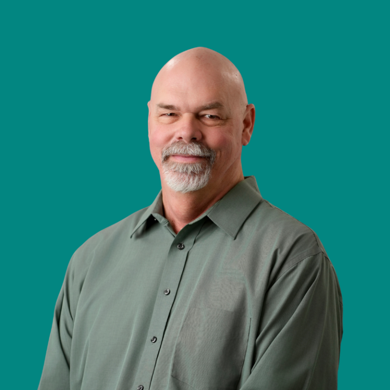 Bald man with goatee wearing olive green button-up shirt against teal background
