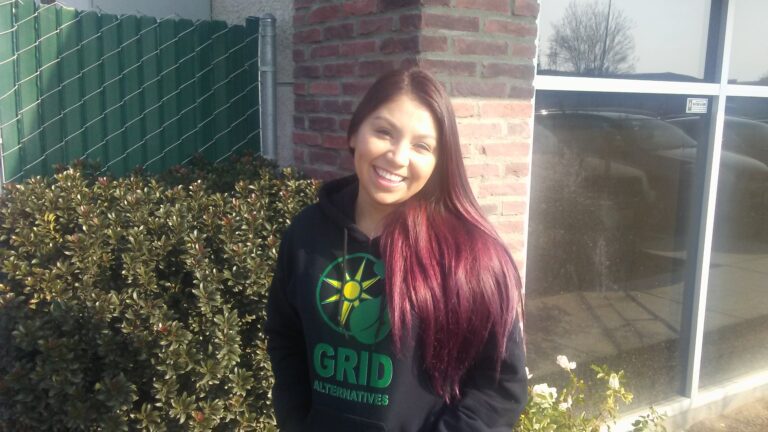 Woman with long burgundy hair smiling outdoors wearing GRID Alternatives black hoodie