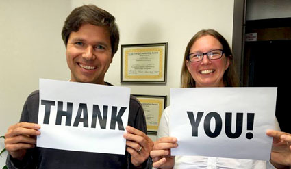 Two people holding signs reading "Thank you!" in an office setting