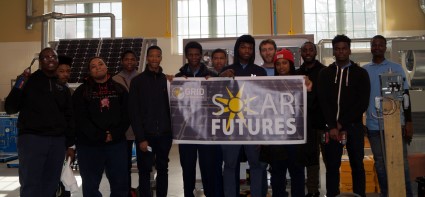 Group of people holding a "Solar Futures" banner indoors with bright windows in background