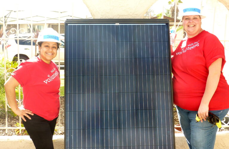 Two volunteers in red shirts holding a large solar panel at an outdoor event