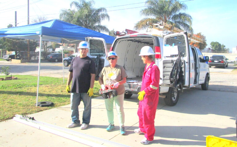 Three workers in hard hats and safety gear stand by a white van during a solar installation project