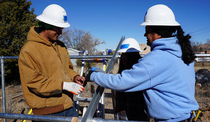 Three workers in hard hats reviewing construction plans at a solar installation site