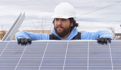 Worker in hard hat installing solar panels on rooftop