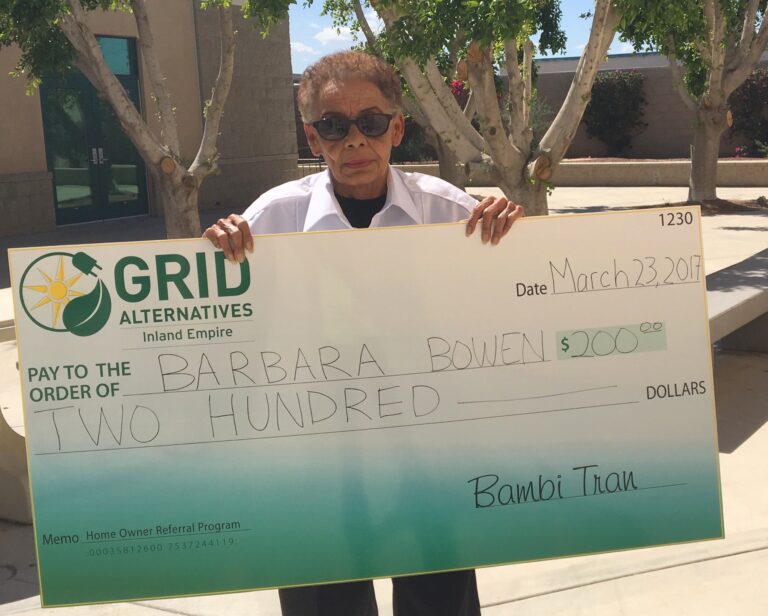 Woman holding large check for $200 from GRID Alternatives Inland Empire, dated March 23, 2017, payable to Barbara Bowen for home owner referral program