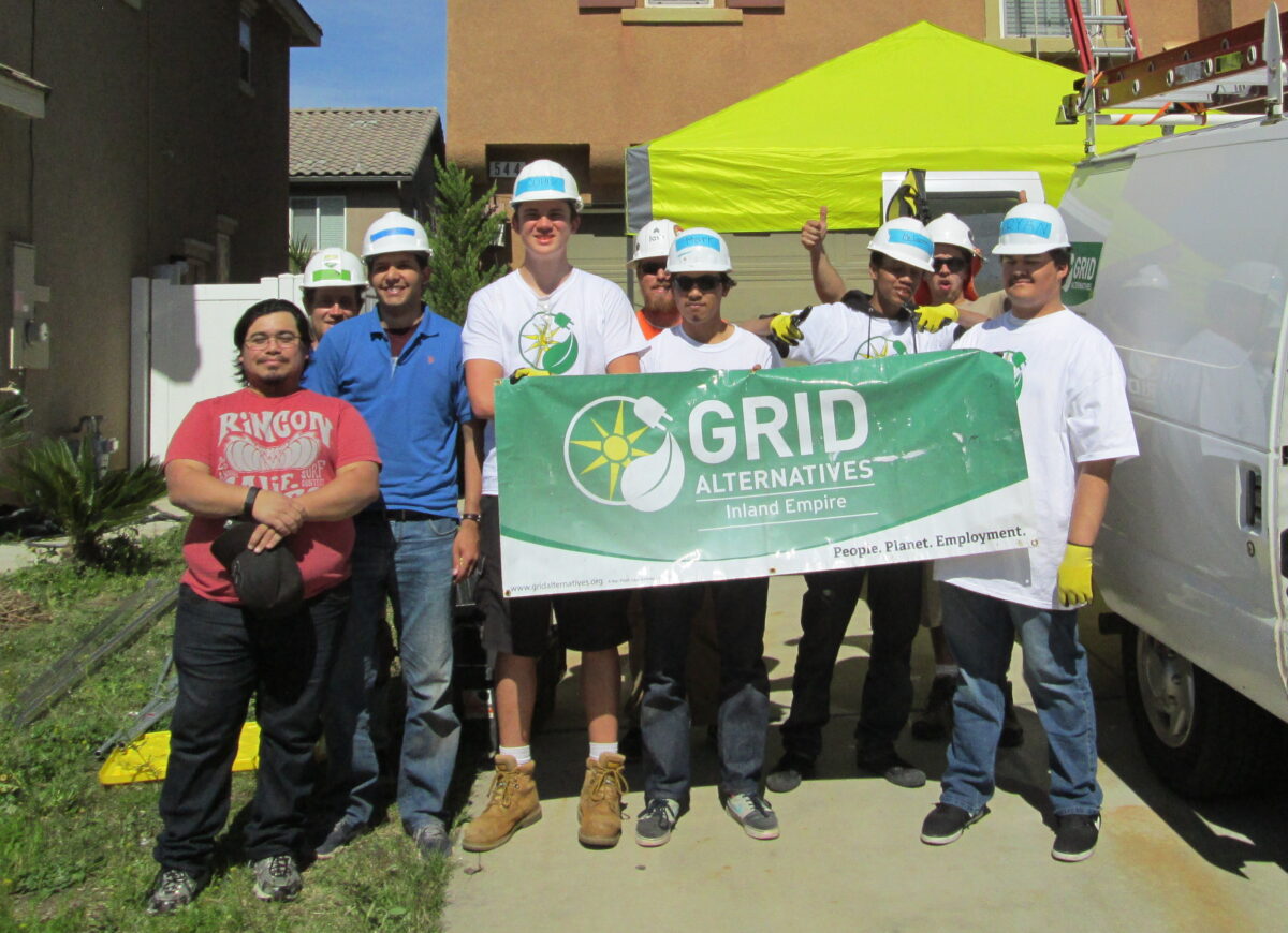 GRID Alternatives Inland Empire team holding banner at community event with volunteers wearing hard hats and safety gear