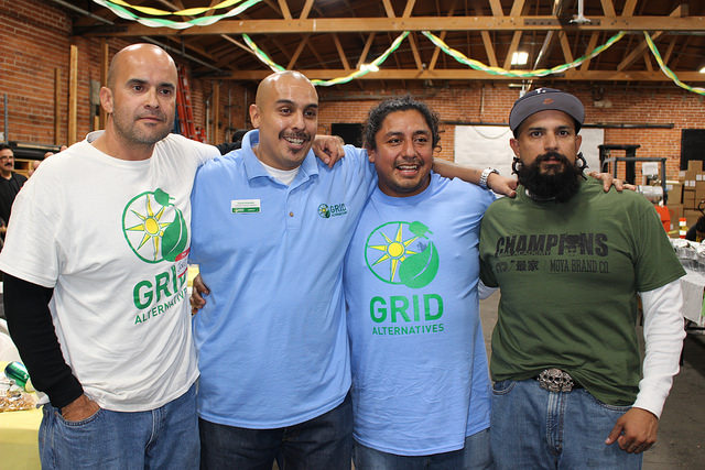 Four men posing together at an indoor event, three wearing GRID Alternatives branded shirts, one wearing a Champions shirt