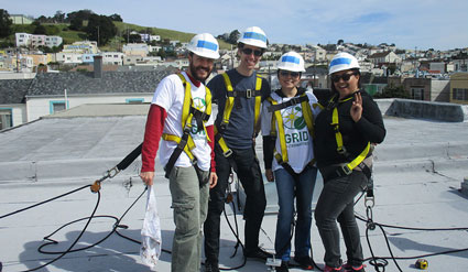 Five workers in hard hats and safety vests stand together on a rooftop during a solar installation project