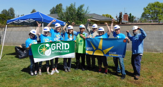 Team of workers in hard hats holding Grid Alternatives and Solar Lanternbee banners outdoors
