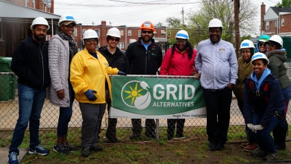 Group of people in hard hats holding GRID Alternatives banner at solar installation site in Baltimore