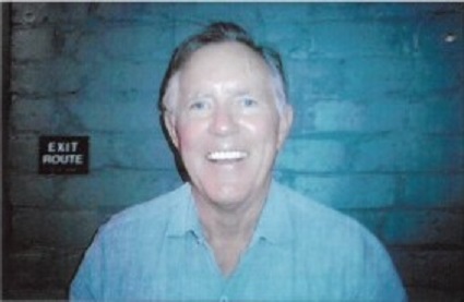 Smiling man in light blue shirt against textured blue background with exit route sign visible