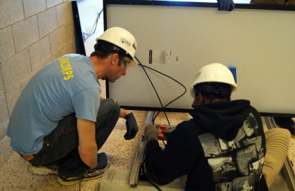 Two workers in hard hats installing solar panel wiring indoors