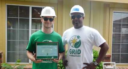 Two volunteers in hard hats holding a certificate and plants outdoors