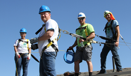 Five construction workers in hard hats installing solar panels on a roof under blue sky