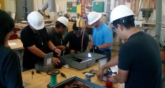 Group of students in hard hats learning woodworking skills at workshop table