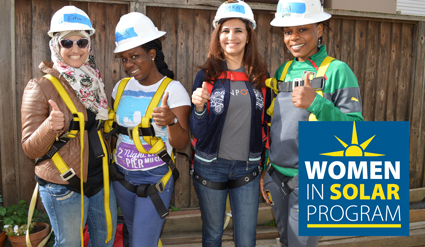 Four women in hard hats and safety gear posing together with Women in Solar Program logo