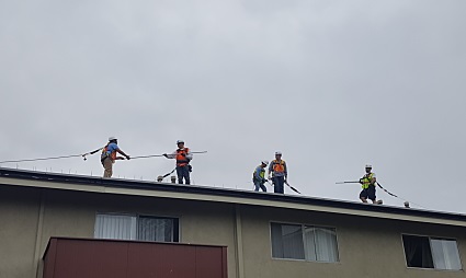 Four workers installing solar panels on a residential rooftop under cloudy skies