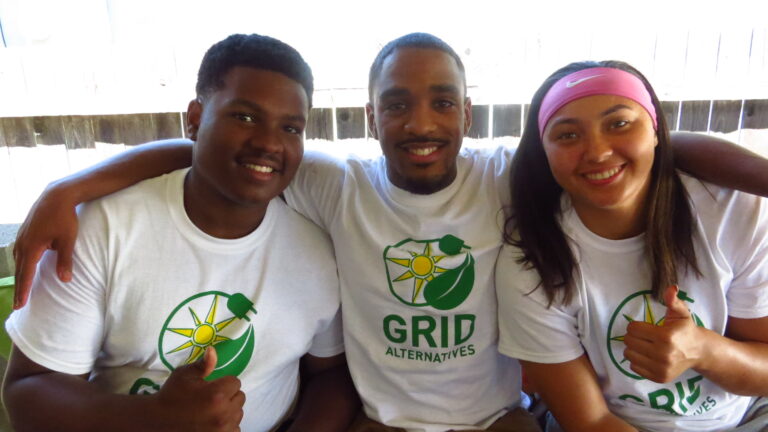 Three smiling students wearing GRID Alternatives t-shirts with solar logo