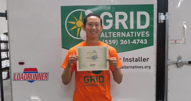 Man in orange GRID Alternatives shirt holds certification certificate in front of branded vehicle