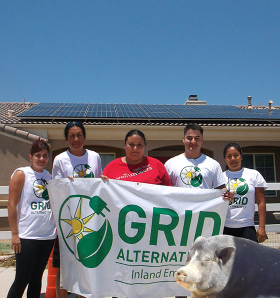 Five people holding GRID Alternatives banner in front of house with solar panels on roof