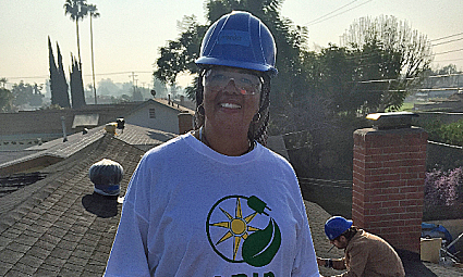 Man in blue hard hat and light blue shirt with circular logo on rooftop with coworkers