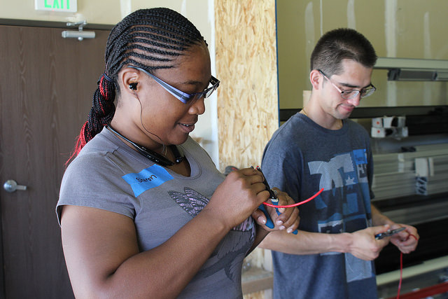 Two young people in matching gray shirts working with electrical wiring during solar training