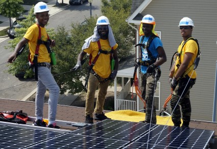 Four workers in safety gear stand on rooftop solar panels during a training session