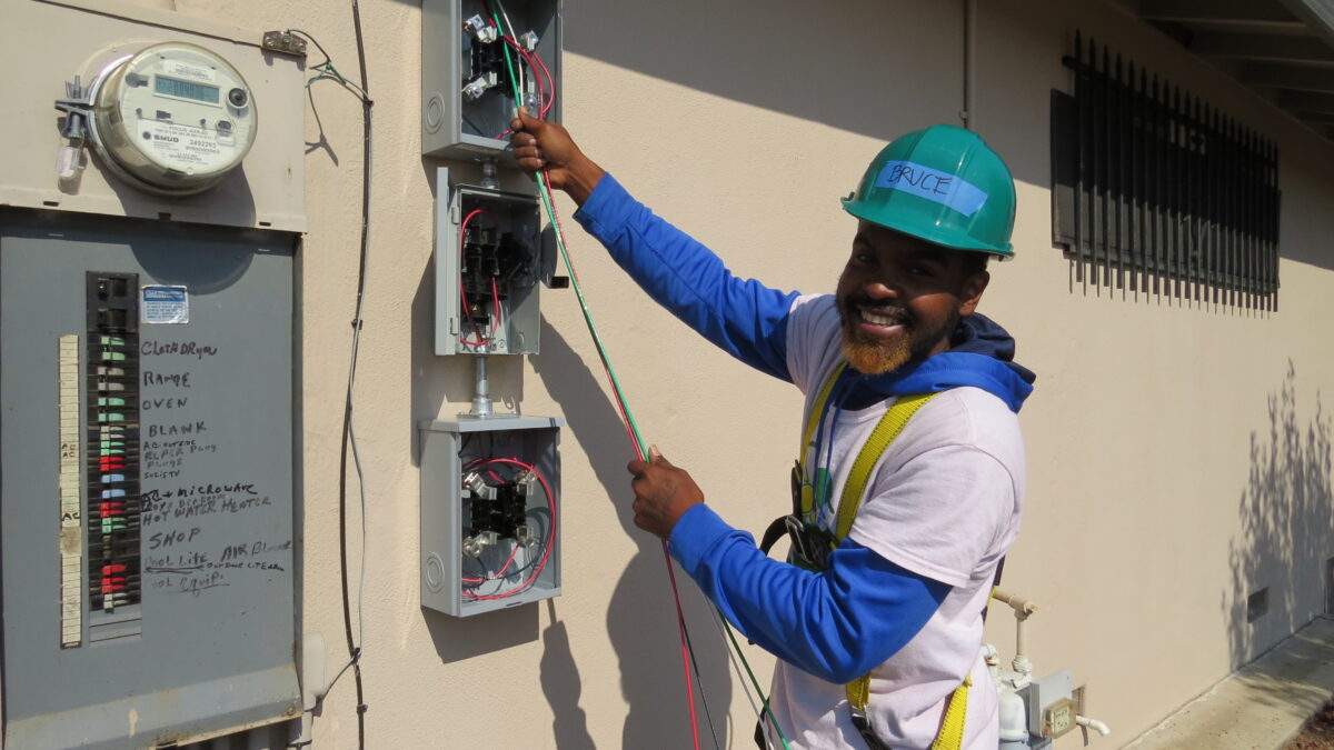 Electrician in safety gear works on residential electrical panel installation on building exterior