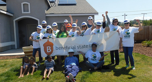 Group of volunteers in hard hats holding "beneficial state" banner at residential solar installation