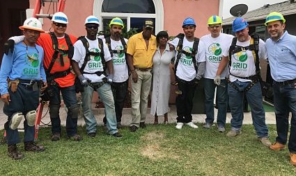 Group of construction workers and professionals wearing hard hats and GRID vests standing together on grass in front of a pink building