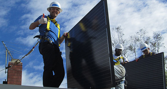 Workers in hard hats installing solar panels on a rooftop under blue sky