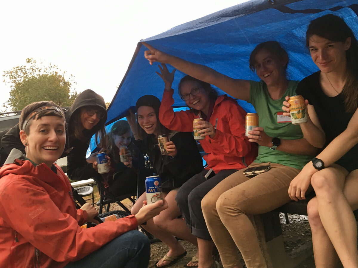 Group of smiling people holding drinks under a blue tent outdoors