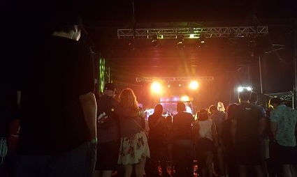 Crowd gathered at indoor concert or event with stage lights illuminated and performers on stage