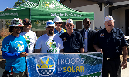 Group of people at outdoor solar initiative event holding "Troops to Solar" banner