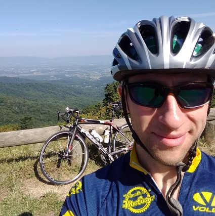 Cyclist in blue and yellow kit at mountain overlook with bike and landscape view