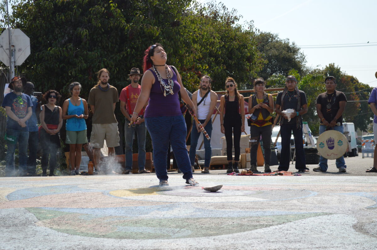 Woman dancing at community block party with spectators gathered around colorful ground designs
