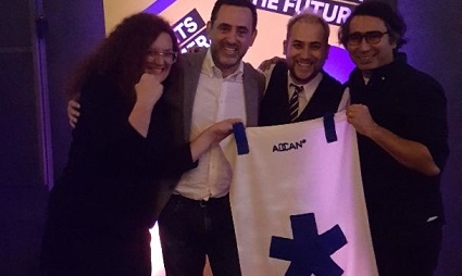 Four people holding a white poster with blue cross symbol at an event with purple lighting