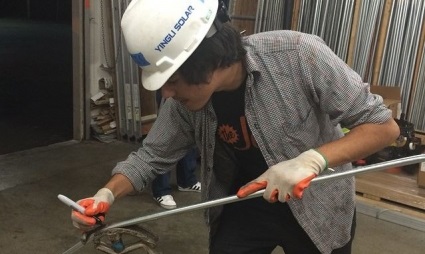 Worker in hard hat and safety gloves using a cutting tool on metal pipe