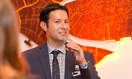 Man in suit speaking at microphone with orange map background