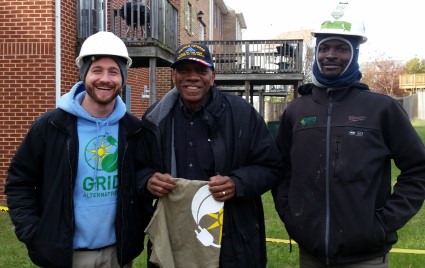 Three men in hard hats and winter clothing stand together outdoors holding a folded flag on Veterans Day